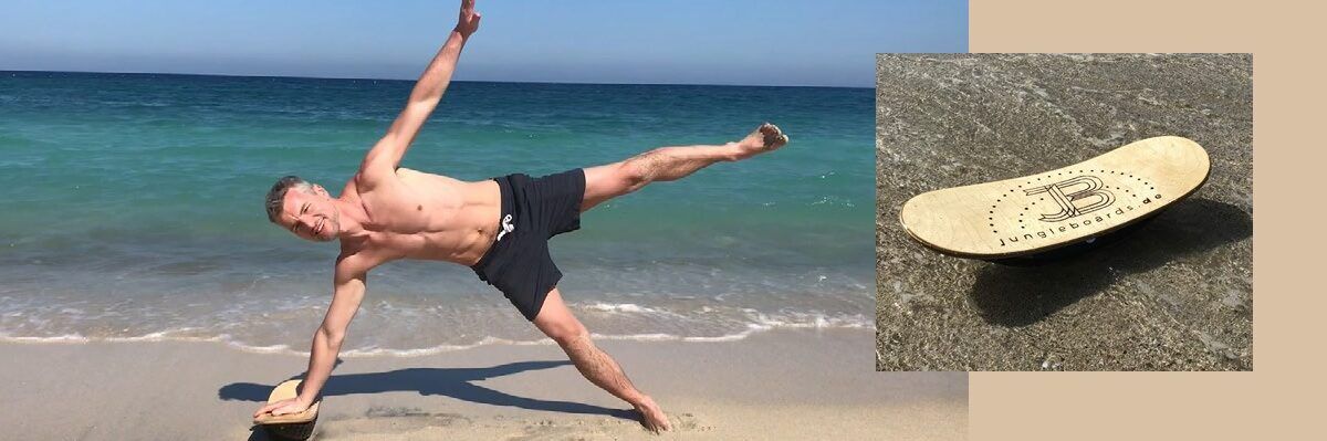 Michael Bischoff stützt sich am Strand mit dem rechten Arm auf das Jungleboard für eine Sportübung.